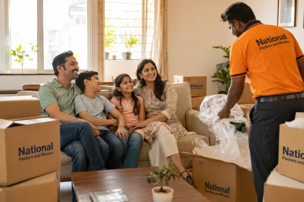 A heartwarming scene inside a newly moved-into Mumbai apartment. A happy Indian family of four sits on a reassembled sofa surrounded by a few empty branded b…
